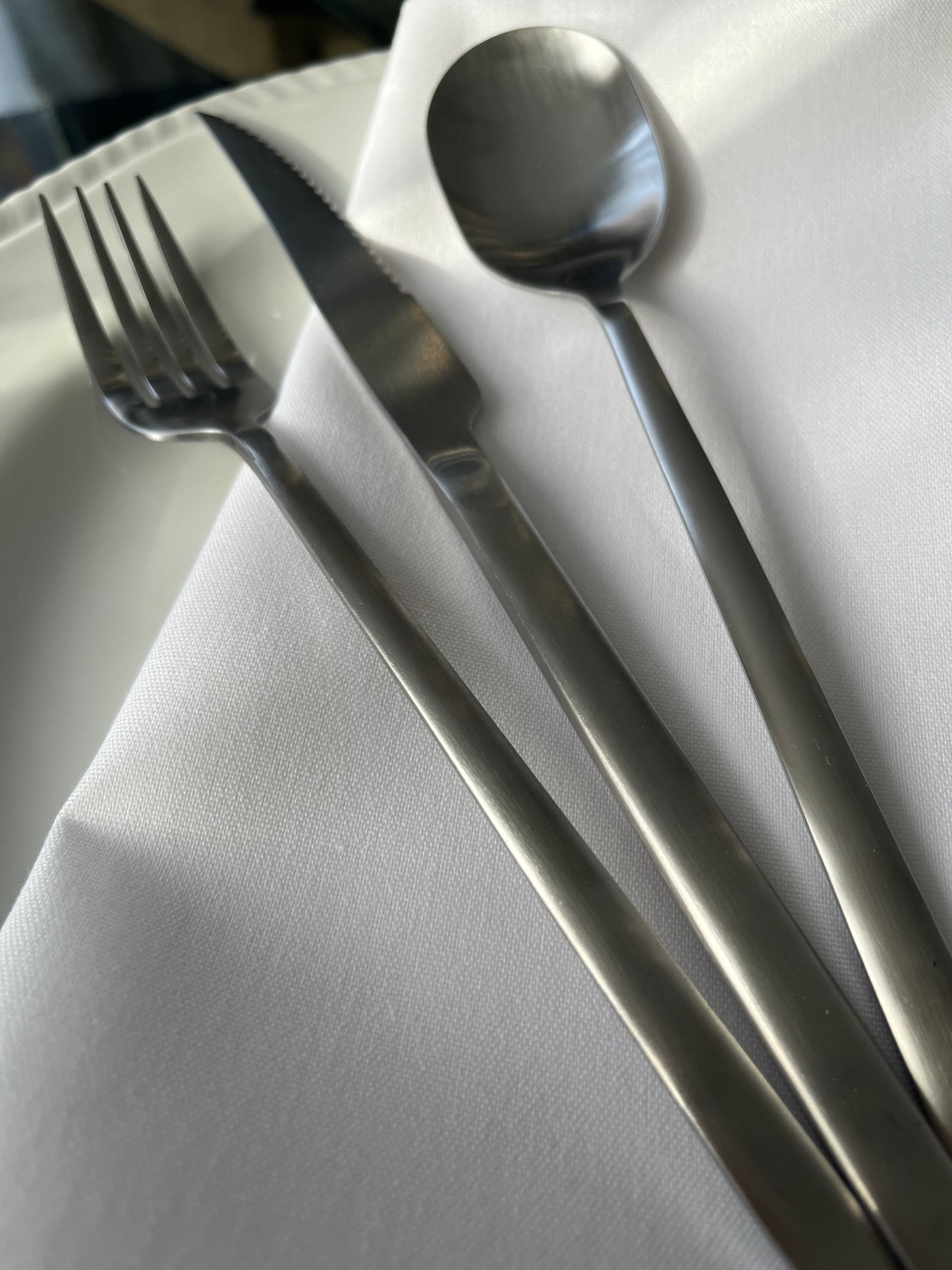 Avie 16-piece matte finish stainless steel cutlery set with forks, knives, spoons, and teaspoons neatly arranged on a modern dining table