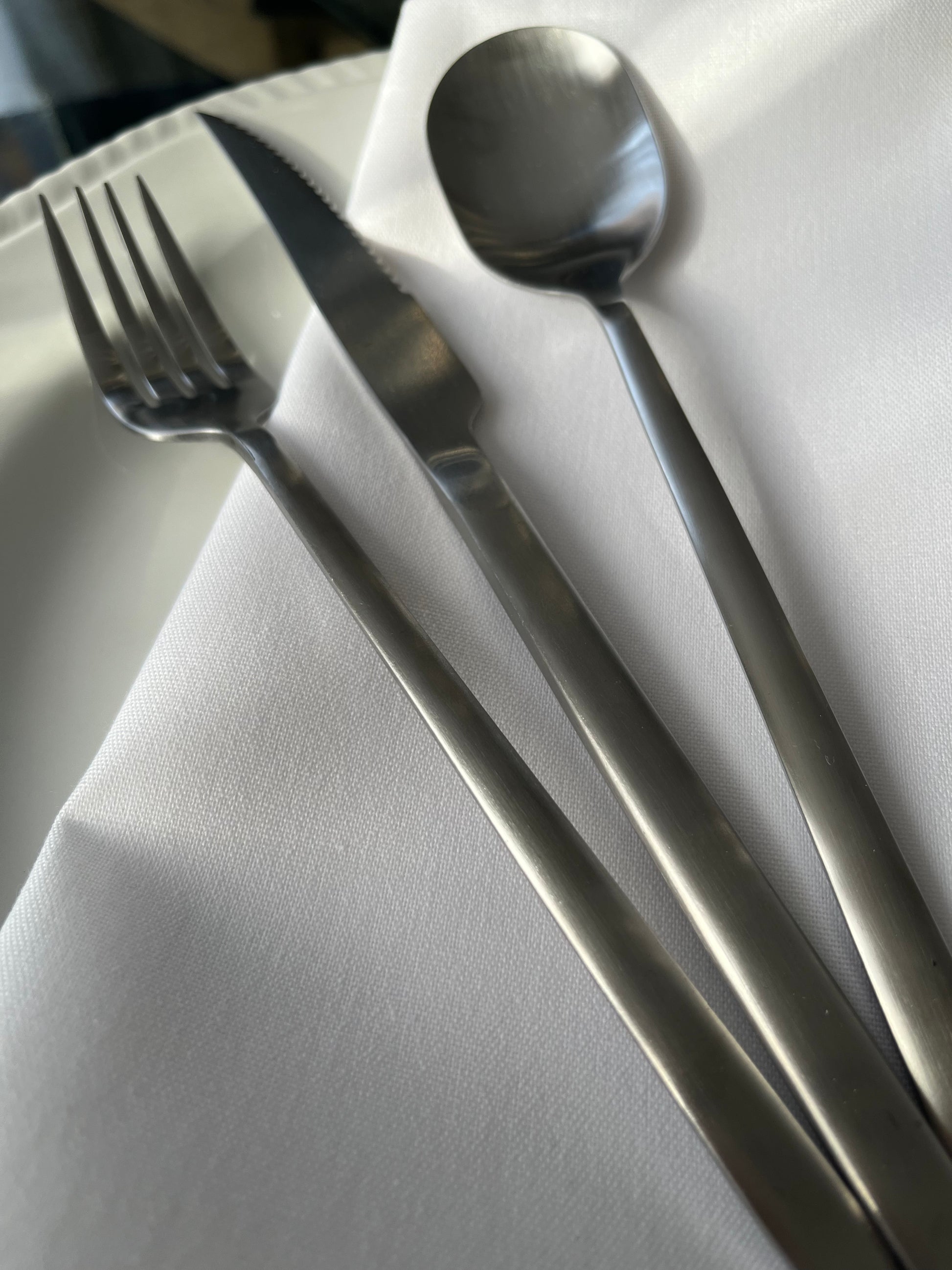Avie 16-piece matte finish stainless steel cutlery set with forks, knives, spoons, and teaspoons neatly arranged on a modern dining table