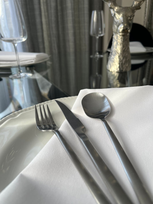 Avie 16-piece matte finish stainless steel cutlery set with forks, knives, spoons, and teaspoons neatly arranged on a modern dining table